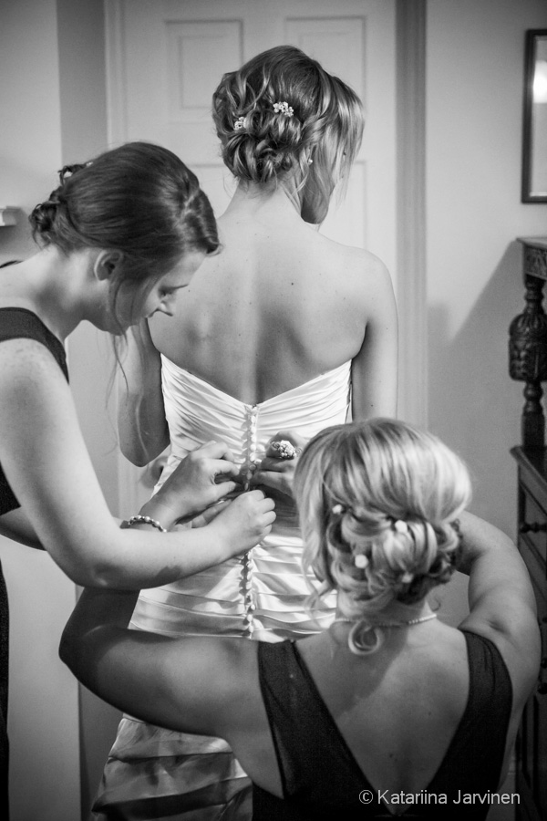 bridesmaids helping bride put on wedding dress